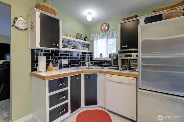 kitchen with tasteful backsplash, freestanding refrigerator, open shelves, white dishwasher, and a sink