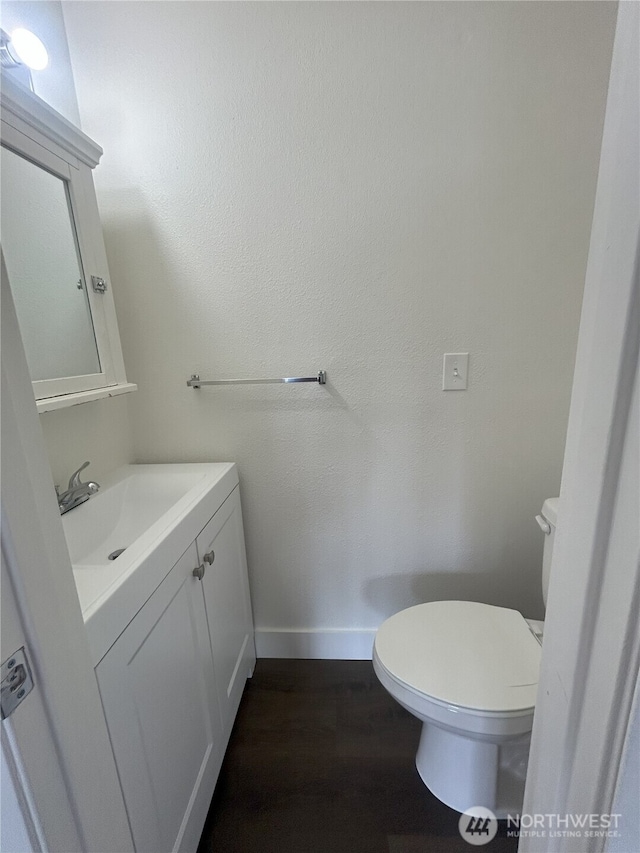 half bath featuring baseboards, wood finished floors, toilet, and vanity