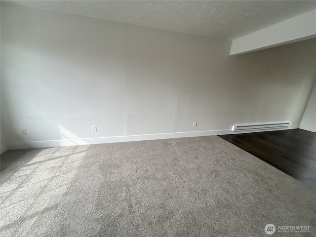 empty room featuring baseboards, a baseboard heating unit, and dark colored carpet