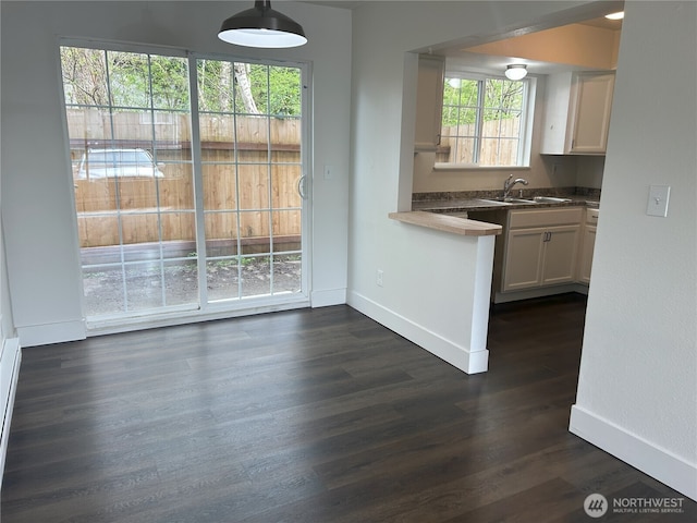 kitchen with hanging light fixtures, dark wood finished floors, a sink, baseboards, and white cabinets