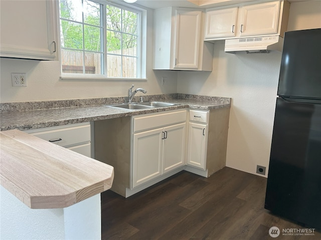 kitchen with freestanding refrigerator, dark wood-style flooring, white cabinetry, under cabinet range hood, and a sink
