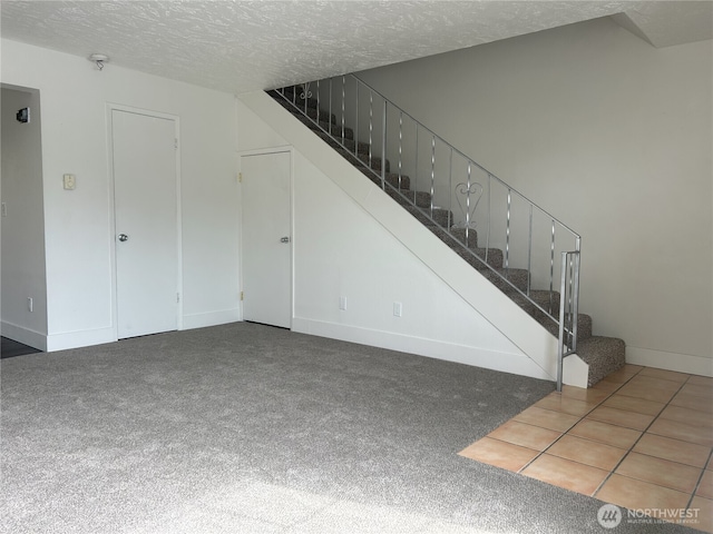 unfurnished living room featuring baseboards, carpet, a textured ceiling, and stairway