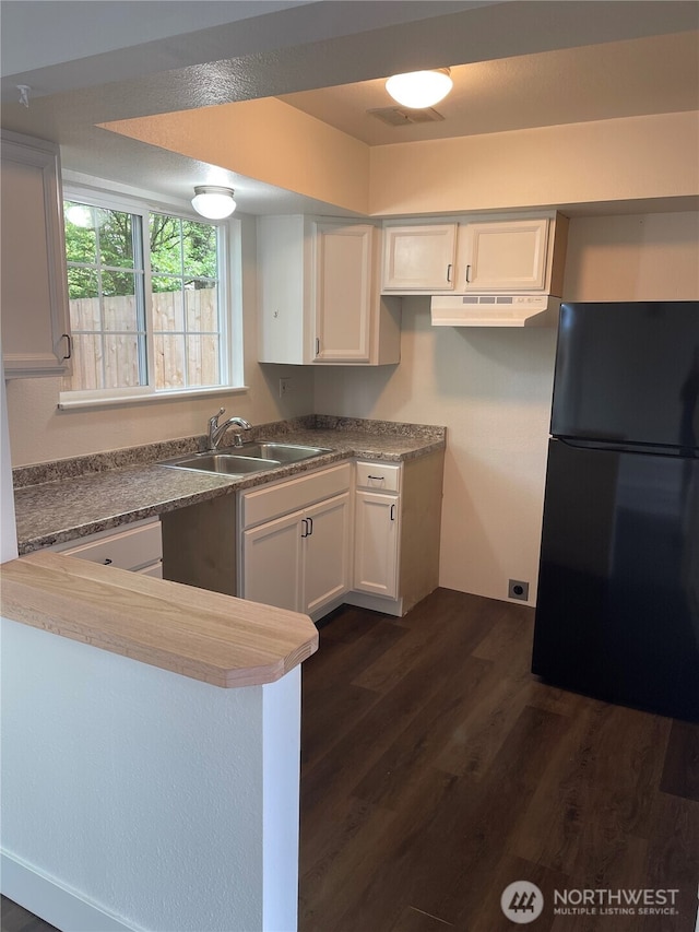 kitchen featuring dark wood-style flooring, a sink, white cabinets, freestanding refrigerator, and under cabinet range hood