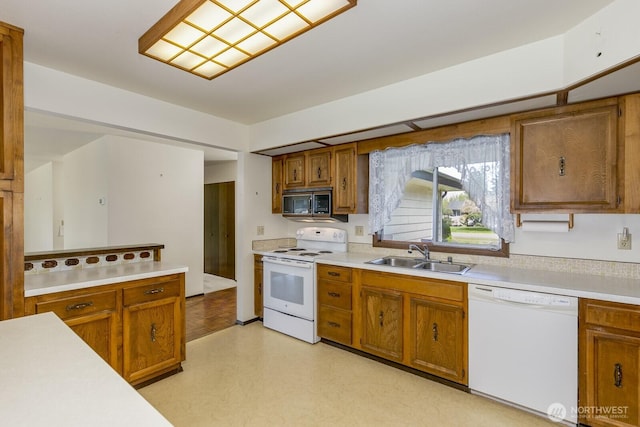 kitchen featuring brown cabinets, a sink, light countertops, light floors, and white appliances