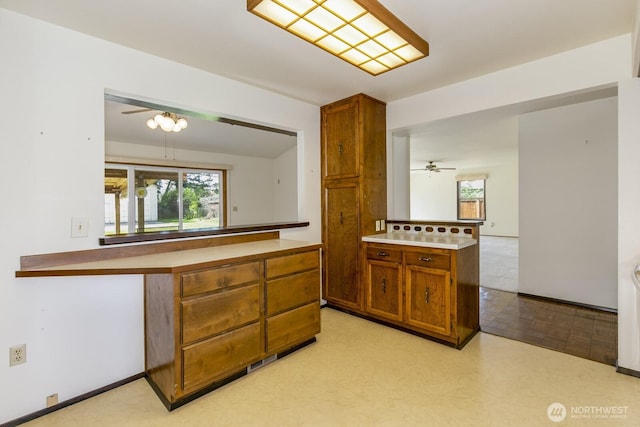 kitchen featuring ceiling fan, a peninsula, light countertops, and brown cabinetry