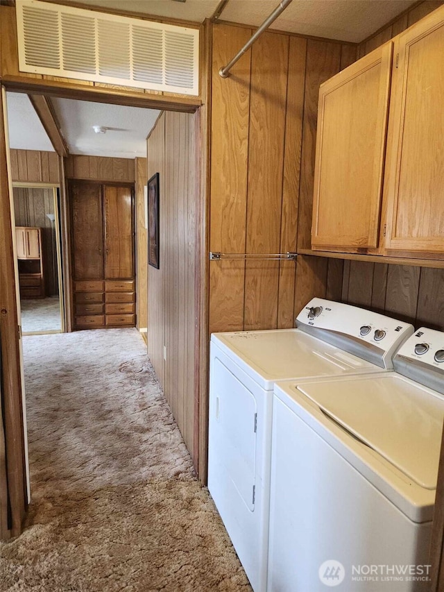 clothes washing area with independent washer and dryer, wooden walls, cabinet space, and carpet