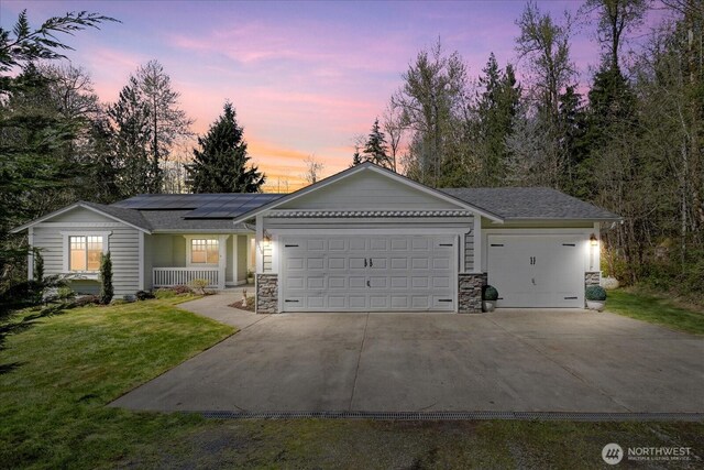 ranch-style house featuring a front lawn, driveway, an attached garage, a porch, and solar panels