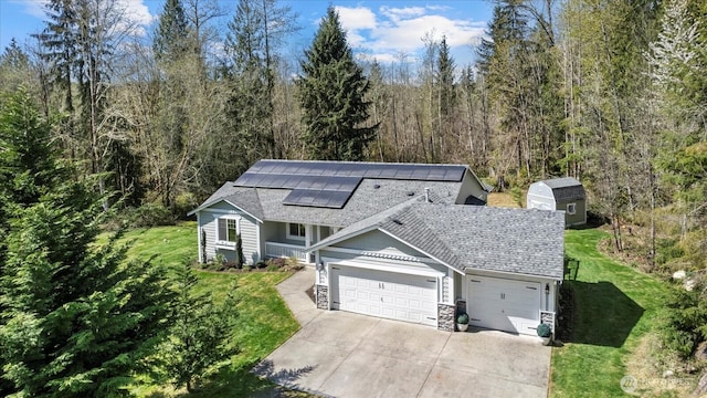 view of front of house featuring roof mounted solar panels, a front lawn, concrete driveway, roof with shingles, and a garage
