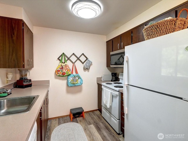 kitchen featuring a sink, light countertops, baseboards, light wood finished floors, and white appliances
