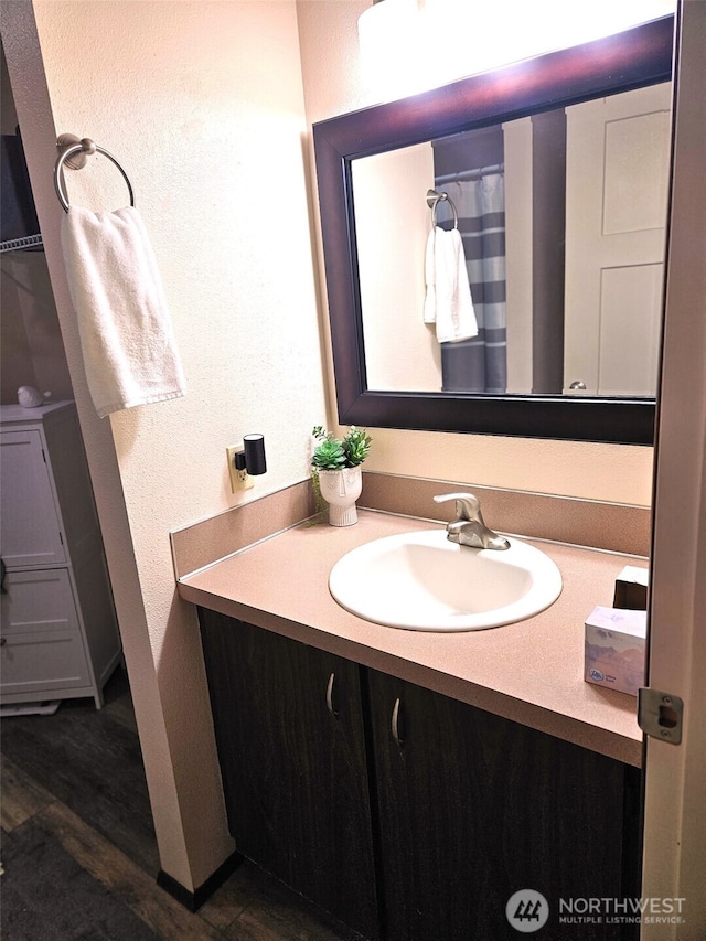 full bath featuring vanity, a textured wall, and wood finished floors