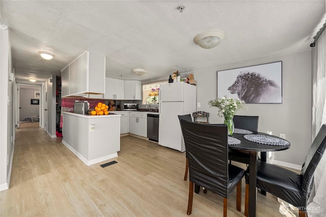 kitchen with visible vents, light wood-type flooring, freestanding refrigerator, a textured ceiling, and stainless steel dishwasher