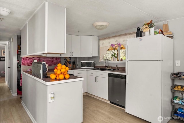 kitchen with white cabinets, dishwasher, a sink, freestanding refrigerator, and light wood finished floors