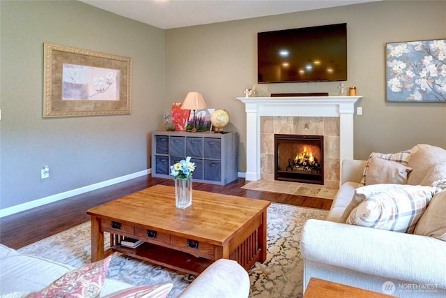 living room with wood finished floors, a tile fireplace, and baseboards