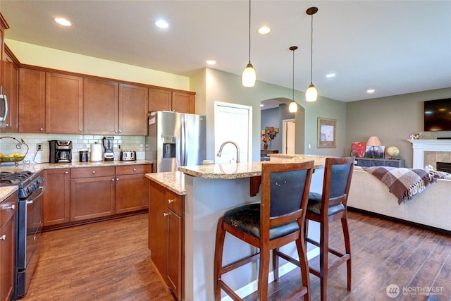 kitchen with appliances with stainless steel finishes, arched walkways, dark wood finished floors, a kitchen bar, and recessed lighting