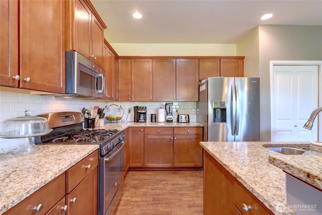 kitchen featuring appliances with stainless steel finishes, a sink, light wood-type flooring, brown cabinetry, and recessed lighting