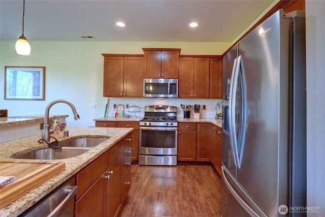 kitchen featuring appliances with stainless steel finishes, a sink, brown cabinets, dark wood-type flooring, and light stone counters