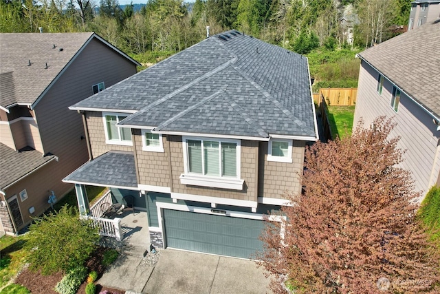 view of front of property with a shingled roof, a garage, concrete driveway, fence, and covered porch