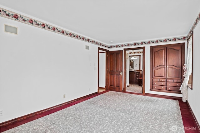 unfurnished bedroom featuring visible vents, baseboards, dark colored carpet, and ensuite bathroom