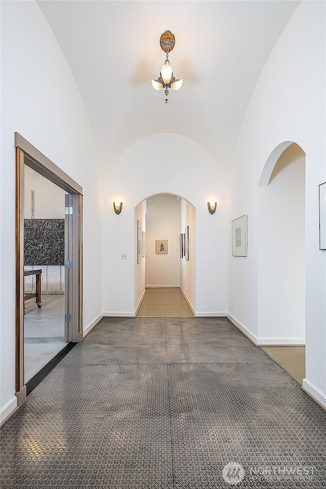 hallway with arched walkways, baseboards, and vaulted ceiling