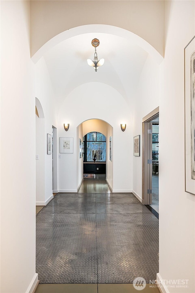 hall with arched walkways, baseboards, and lofted ceiling