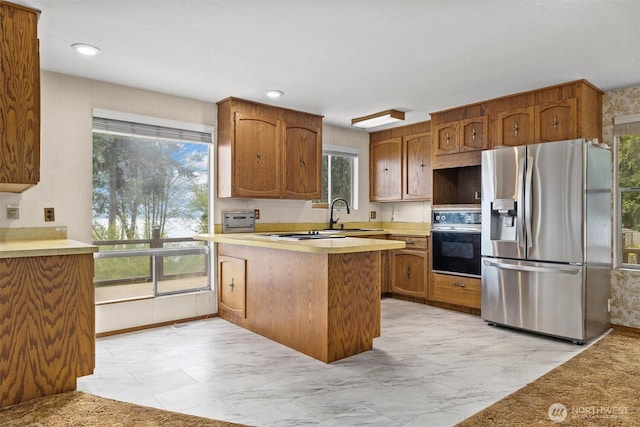 kitchen featuring a peninsula, oven, a healthy amount of sunlight, and stainless steel fridge