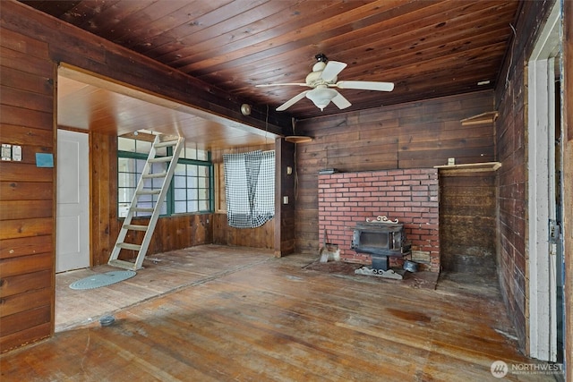 unfurnished living room featuring wooden walls, a wood stove, wood ceiling, hardwood / wood-style flooring, and ceiling fan