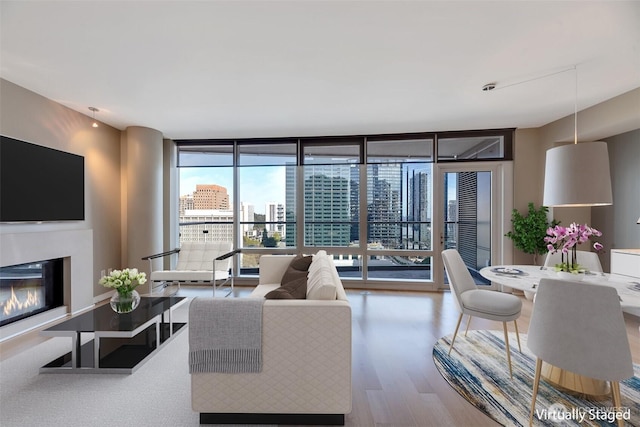 living area featuring a city view, wood finished floors, a glass covered fireplace, and expansive windows