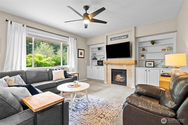 living area featuring carpet flooring, ceiling fan, a tile fireplace, baseboards, and built in features