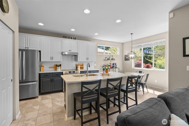 kitchen with appliances with stainless steel finishes, a sink, backsplash, a breakfast bar area, and hanging light fixtures