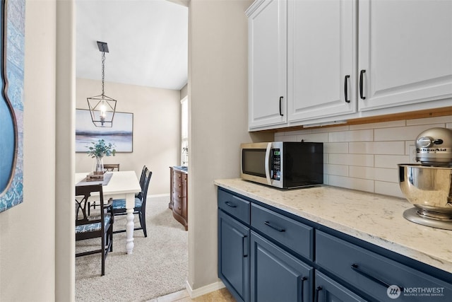 kitchen featuring stainless steel microwave, blue cabinets, white cabinets, decorative backsplash, and baseboards