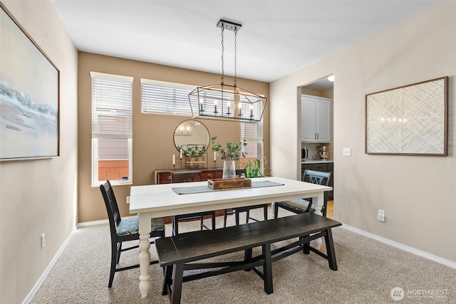 dining area with a chandelier, light colored carpet, and baseboards