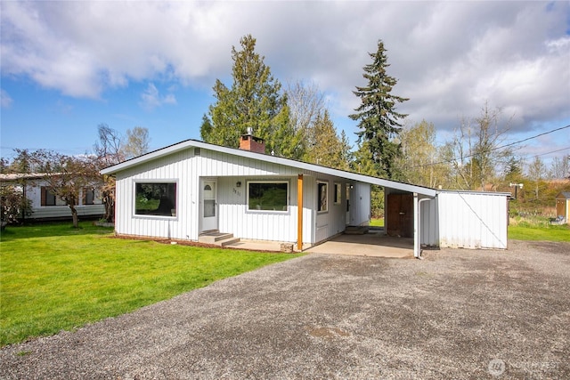 view of front facade with a carport, a chimney, driveway, board and batten siding, and a front lawn