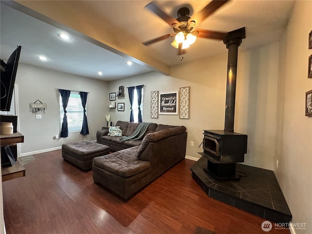living room featuring dark wood-style floors, a wood stove, baseboards, and a ceiling fan