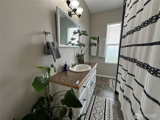 bathroom with curtained shower, vanity, baseboards, and stone tile flooring