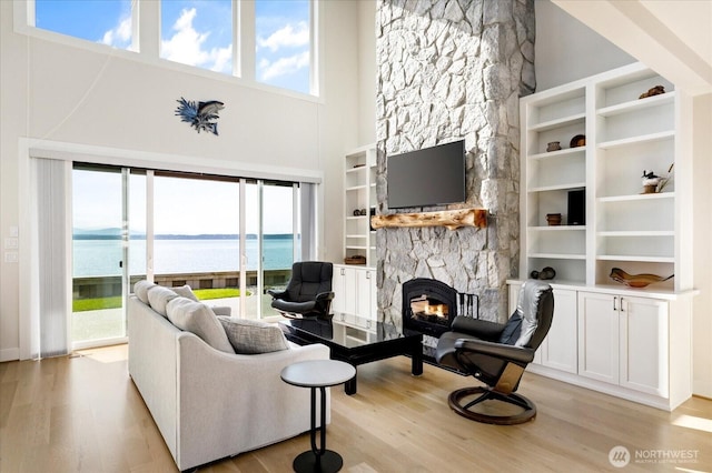 living room with a fireplace, plenty of natural light, a towering ceiling, and light wood-style flooring