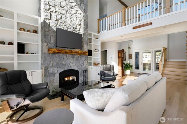 living area with wood finished floors, a high ceiling, a stone fireplace, and stairway