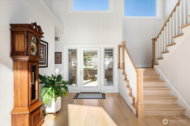 foyer with wood finished floors, a towering ceiling, plenty of natural light, and stairway