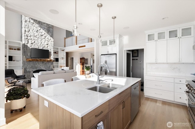 kitchen featuring glass insert cabinets, a sink, light wood-type flooring, appliances with stainless steel finishes, and a kitchen island with sink