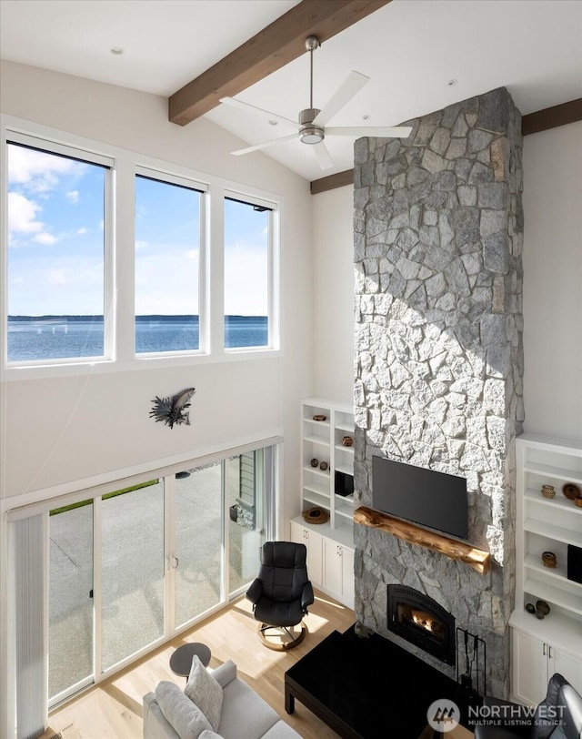 living area featuring a wealth of natural light, light wood finished floors, a stone fireplace, and lofted ceiling with beams