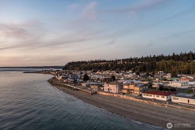 aerial view at dusk featuring a water view and a beach view