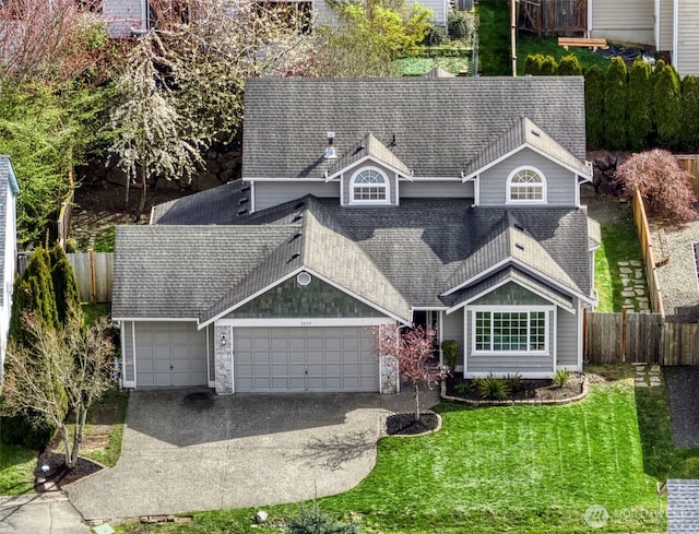 view of front of property featuring driveway, a shingled roof, a front yard, an attached garage, and fence