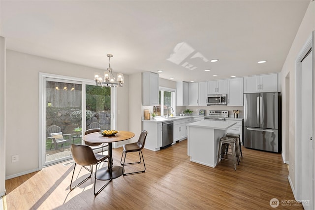 kitchen with a chandelier, appliances with stainless steel finishes, light countertops, a sink, and a center island
