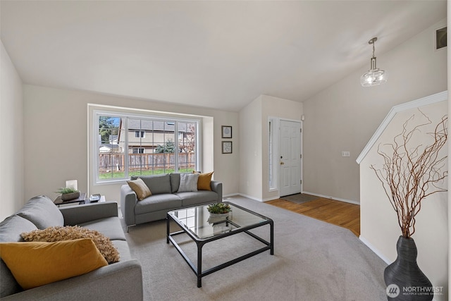 carpeted living area featuring lofted ceiling, wood finished floors, and baseboards