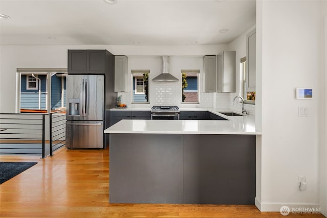 kitchen featuring appliances with stainless steel finishes, a sink, wall chimney range hood, gray cabinets, and tasteful backsplash