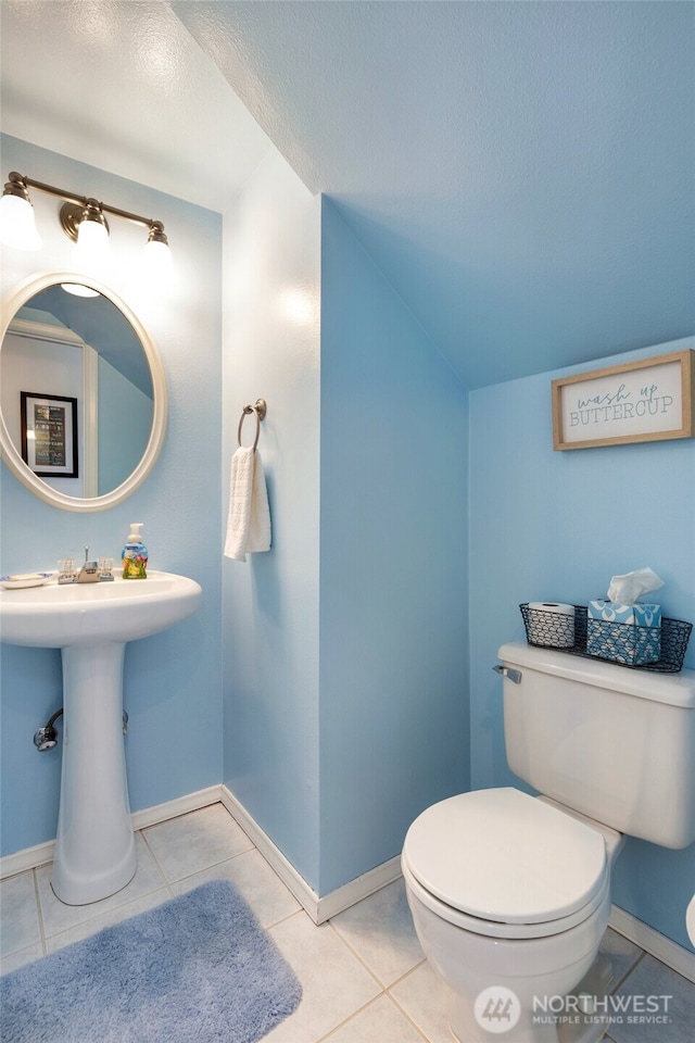 bathroom with toilet, a textured ceiling, vaulted ceiling, tile patterned flooring, and baseboards