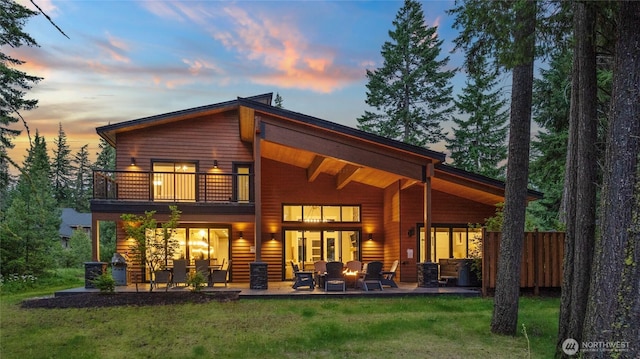 back of property at dusk featuring a lawn, outdoor lounge area, a patio area, and a balcony