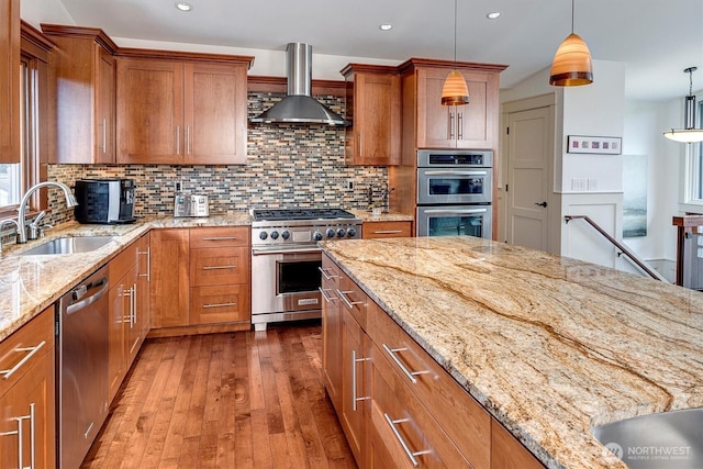 kitchen with stainless steel appliances, brown cabinets, wall chimney exhaust hood, and a sink
