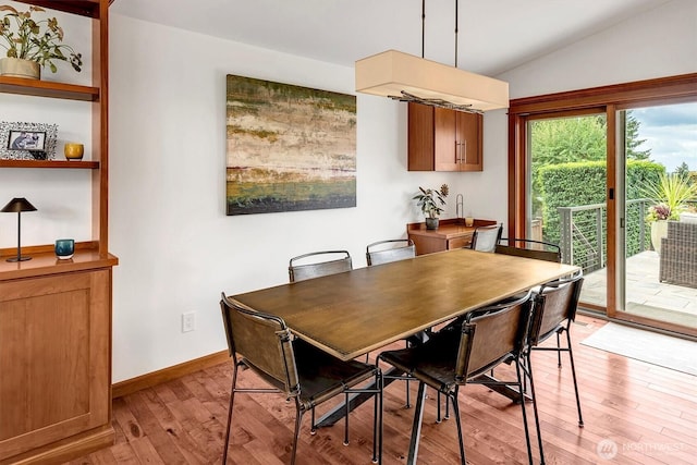 dining room with light wood finished floors, baseboards, and vaulted ceiling