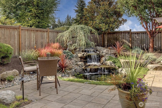 view of patio / terrace featuring a garden pond, a fenced backyard, and outdoor dining area