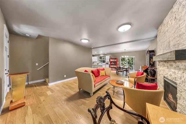 living room featuring baseboards, an inviting chandelier, a fireplace, and light wood-type flooring